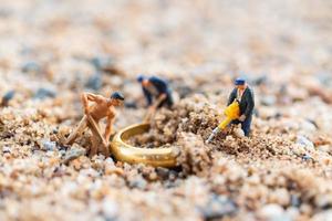 miniatuurarbeiders die gouden ringen in het zand, bedrijfsgroeiconcept graven foto