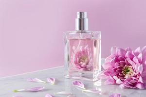 een transparant fles van kunstmatig verstuiven of parfum tegen een mooi lila bloemen. aroma presentatie. roze achtergrond met een kopiëren ruimte. foto