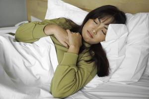 een verdrietig jong Aziatisch vrouw is huilen terwijl aan het liegen Aan de bed foto