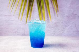 blauw hawaiiaans drinken in een plastic glas en kokosnoot bladeren. foto