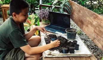 jongen leert naar toenemen bloemen in potten door online onderwijs. scheppen bodem in potten naar bereiden planten voor aanplant vrije tijd activiteiten concept foto