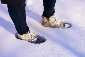 vrouwen voeten in licht suede laarzen en blauw jeans zijn staand in de sneeuw foto