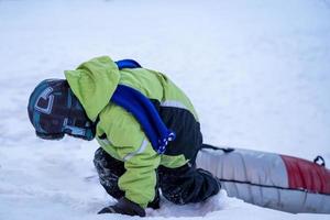 grappig Kaukasisch jongen 5 jaren oud ritten in winter Aan een groot opblaasbaar kwarktaart foto