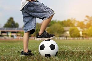 Aziatisch jongen stepping Aan een bal terwijl schoppen voetbal Aan de veld. zacht en selectief focus. foto