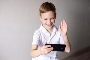 een jongen in een wit t-shirt met een zwart telefoon communiceert via video babbelen foto