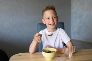 schattig jongen eet een droog ontbijt Bij huis en glimlacht foto