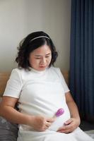 jong Aziatisch zwanger vrouw gebruik makend van rammelaar speelgoed- naar Speel met haar ongeboren baby foto