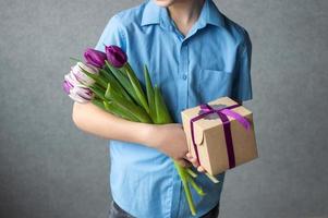 kleurrijk boeket van tulpen met een geschenk doos in de handen van een kind. foto