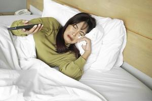 een verdrietig jong Aziatisch vrouw is huilen over- haar telefoon terwijl aan het liegen Aan de bed foto