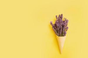 lavendel bloemen in een wafel ijshoorntje Aan een geel achtergrond. minimaal zomer of voorjaar concept foto