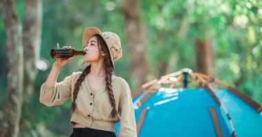 jong vrouw juichen en drinken drank voorkant van camping tent foto