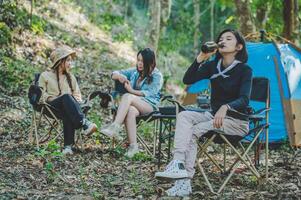 jong Dames zittend en drinken drank voorkant van camping tent foto