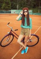 meisje hipster staand met magenta fiets Aan de tennis rechtbank foto