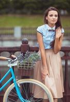 jong mooi, elegant gekleed vrouw met fiets in de park of buitenshuis foto