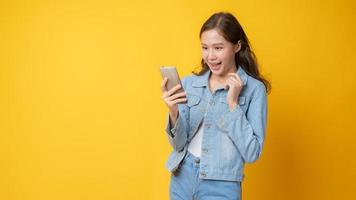 Aziatische vrouw glimlachend en kijken naar mobiele telefoon op gele achtergrond