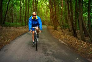 middelbare leeftijd Mens is rijden een weg fiets langs een Woud weg foto