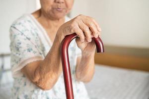 Aziatisch ouderen onbekwaamheid vrouw Holding wandelen stok, hout riet, ronde handvat, wandelen steun voor helpen naar wandelen. foto