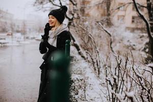 jong vrouw in warm kleren gebruik makend van mobiel telefoon Aan een winter dag foto