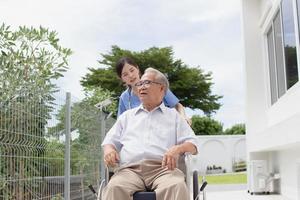 verpleging huis zorg concept. Aziatisch jong verpleegster gehandicapt ouderen Mens. verpleegster, zorg huis en ouderen Mens met onbekwaamheid in een rolstoel in een buiten medisch faciliteit. foto