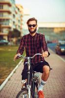 Mens in zonnebril rijden een fiets Aan stad straat foto