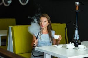 mooi vrouw roken een hookah en drinken thee in een cafe foto