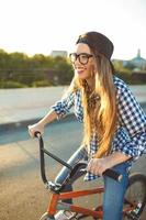 lief jong vrouw in een hoed rijden een fiets Aan stad achtergrond in de zonlicht buitenshuis foto