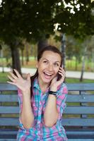 een portret van een glimlachen mooi vrouw in de park pratend Aan de telefoon foto