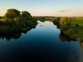 silhouet van een visser in een boot Aan een rivier- Bij zonsondergang foto