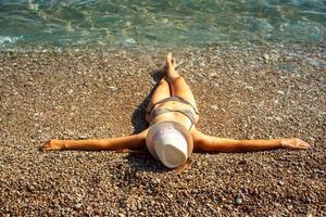 jong vrouw in een hoed en bikini aan het liegen Aan de strand in heet zomer dag foto