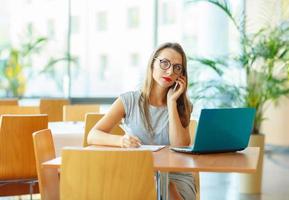 mooi jong vrouw werken met een laptop en pratend Aan de cel telefoon foto