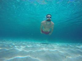 jong baard Mens met bril duiken in een blauw schoon water foto