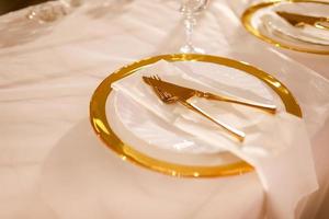 tafel decoratie met roze tafelkleed, kristal kandelaars met kaarsen en wit roze bloemen in restaurant . elegant bruiloft dag. instelling tafel met goud bord, vork en mes foto