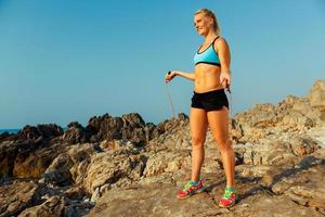 atleet vrouw aan het doen sport oefenen met de touw Aan de rotsen door de zee foto