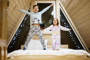 kinderen in zacht warm pyjama spelen Bij houten cabine huis. concept van jeugd, vrije tijd werkzaamheid, geluk. broer en zus hebben pret en spelen samen. foto