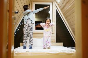 kinderen in zacht warm pyjama spelen Bij houten cabine huis. concept van jeugd, vrije tijd werkzaamheid, geluk. broer en zus hebben pret en spelen samen. foto