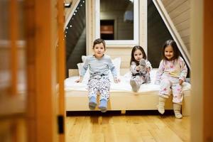 kinderen in zacht warm pyjama spelen Bij houten cabine huis. concept van jeugd, vrije tijd werkzaamheid, geluk. broer en zussen hebben pret en spelen samen. foto