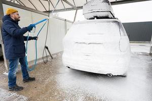 Mens het wassen Amerikaans suv auto met dak rek Bij een zelf onderhoud wassen in verkoudheid het weer. foto