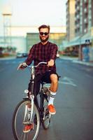 Mens in zonnebril rijden een fiets Aan stad straat foto