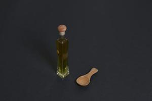 fles van olijf- olie met houten lepel geïsoleerd Aan zwart achtergrond foto