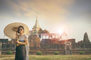 Aziatisch vrouw vervelend Thais traditioneel pak staan met paraplu tegen oud tempel in ayutthaya wereld erfgoed van UNESCO Thailand foto