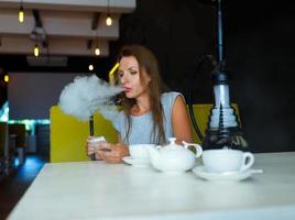mooi vrouw roken een hookah en gebruik makend van smartphone in een cafe foto