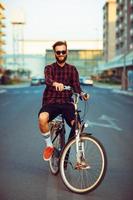 Mens in zonnebril rijden een fiets Aan stad straat foto