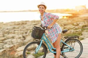 zorgeloos vrouw met fiets rijden Aan een houten pad Bij de zee, hebben pret en glimlachen foto