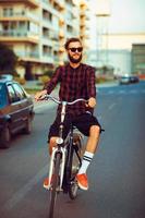 elegant Mens in zonnebril rijden een fiets Aan stad straat foto