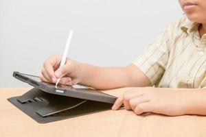 weinig hand- meisje leerling schrijft Aan digitaal tablet naar studie Bij huis. foto