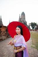 mooi Thais meisje in traditioneel jurk kostuum rood paraplu net zo Thais tempel waar is de openbaar plaats, Thais vrouw in traditioneel kostuum van Thailand. foto