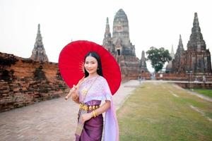 mooi Thais meisje in traditioneel jurk kostuum rood paraplu net zo Thais tempel waar is de openbaar plaats, Thais vrouw in traditioneel kostuum van Thailand. foto