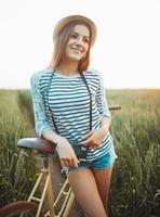 lief jong vrouw staat in een veld- met haar fiets foto