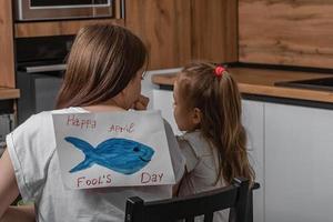mam en dochter zijn zittend in de keuken, Aan de terug van een jong vrouw is een papier vis met de opschrift april dwazen dag. grappig familie grappen, viering. foto