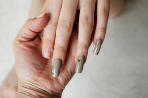 de manicure houdt de hand- van een cliënt met slordig gebroken nagels, met een overwoekerd manicure naar bijwerken foto